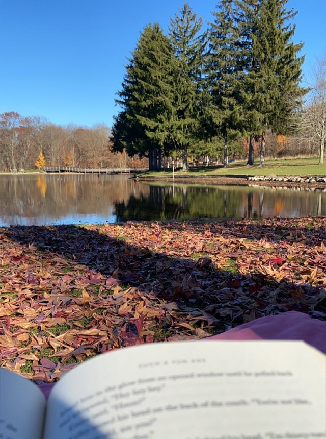 Outside with a book and lake in the background.